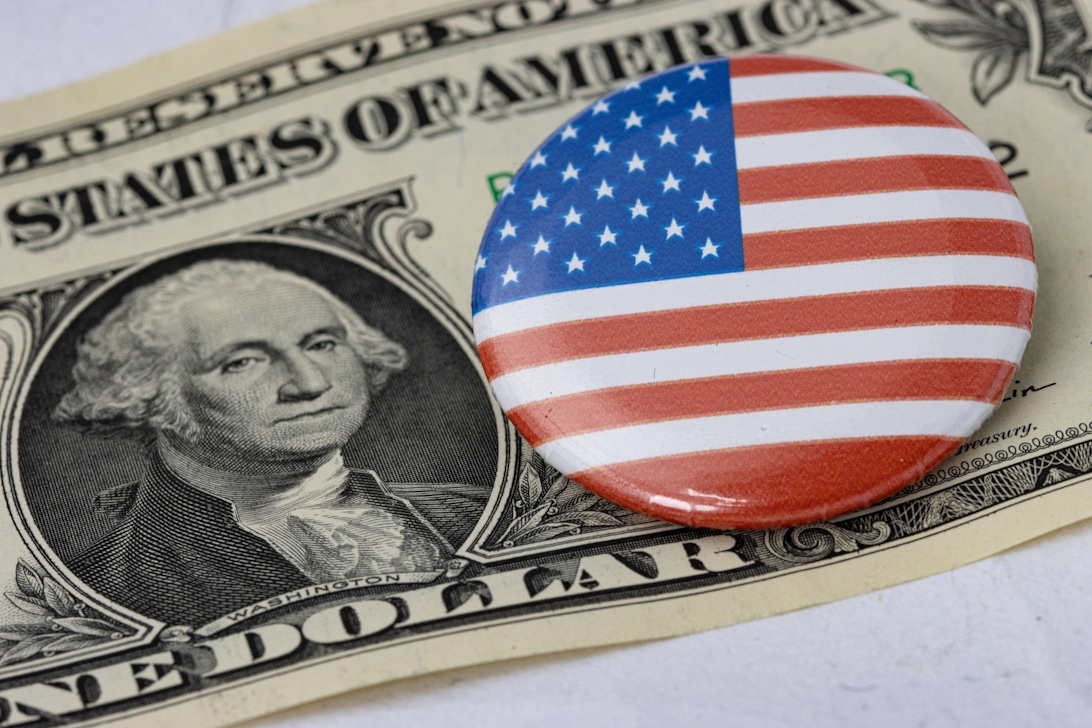 En amerikansk dollarsedel med en knapp med den amerikanska flaggan, vilket symboliserar kopplingen mellan nationell politik och finans.